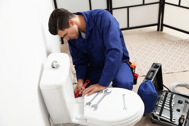 Professional plumber working with toilet bowl in bathroom