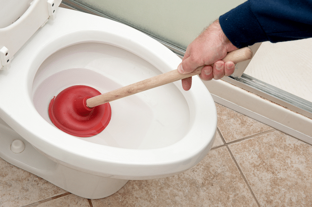 A plumber using a plunger on a toilet