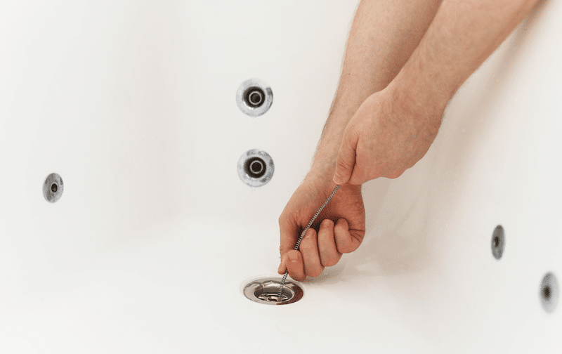 A plumber using a drain snake in a bath tub