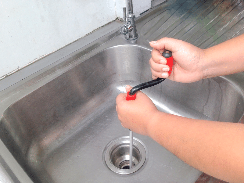 A Man using a plumbing snake in a kitchen drain