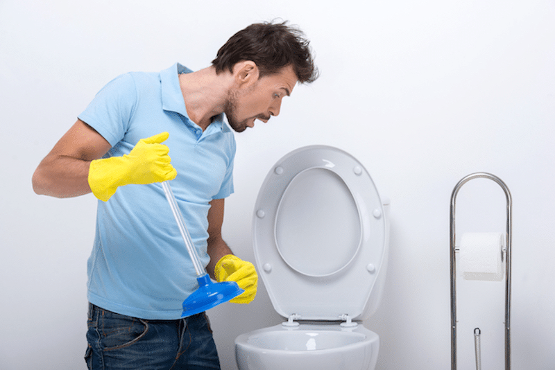 A man using a plunger on his toilet