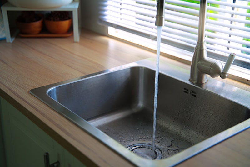 Water running from the tap into a kitchen sink. Clean and drinking water. Save water and enviromental concept.