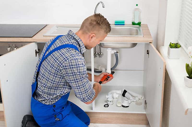 Male Plumber Fixing Sink Pipe With Adjustable Wrench In Kitchen