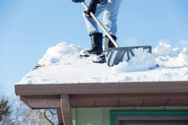 A man is shoveling snow off of a house roof after a Minnesota blizzard.