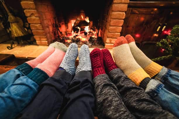 Legs view of happy family wearing warm socks in front of cozy fireplace - Focus on left socks