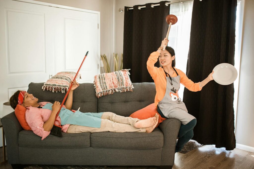 A humorous moment with a couple playfully using cleaning tools in a living room.