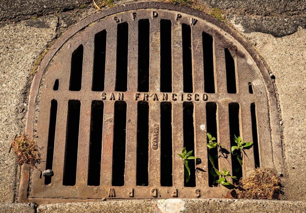 Close-up photo of a weathered drain cover embossed with 'San Francisco', showcasing urban texture and detail.