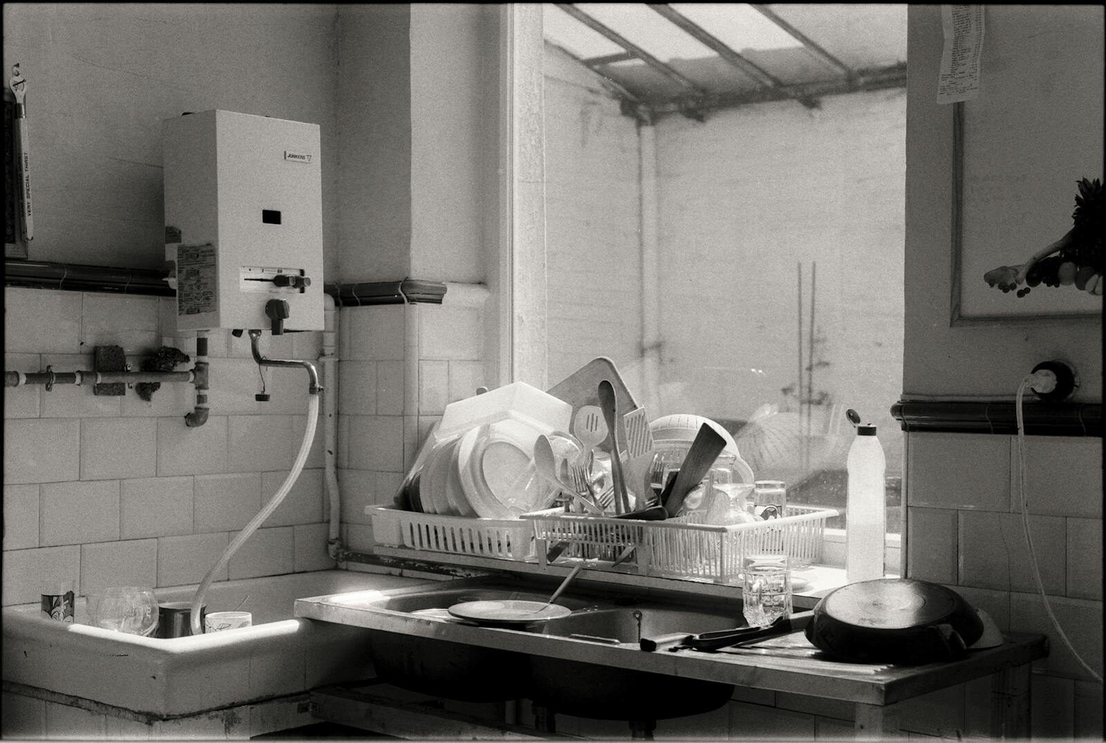 Black and white image of a kitchen sink filled with dishes and cutlery by the window.