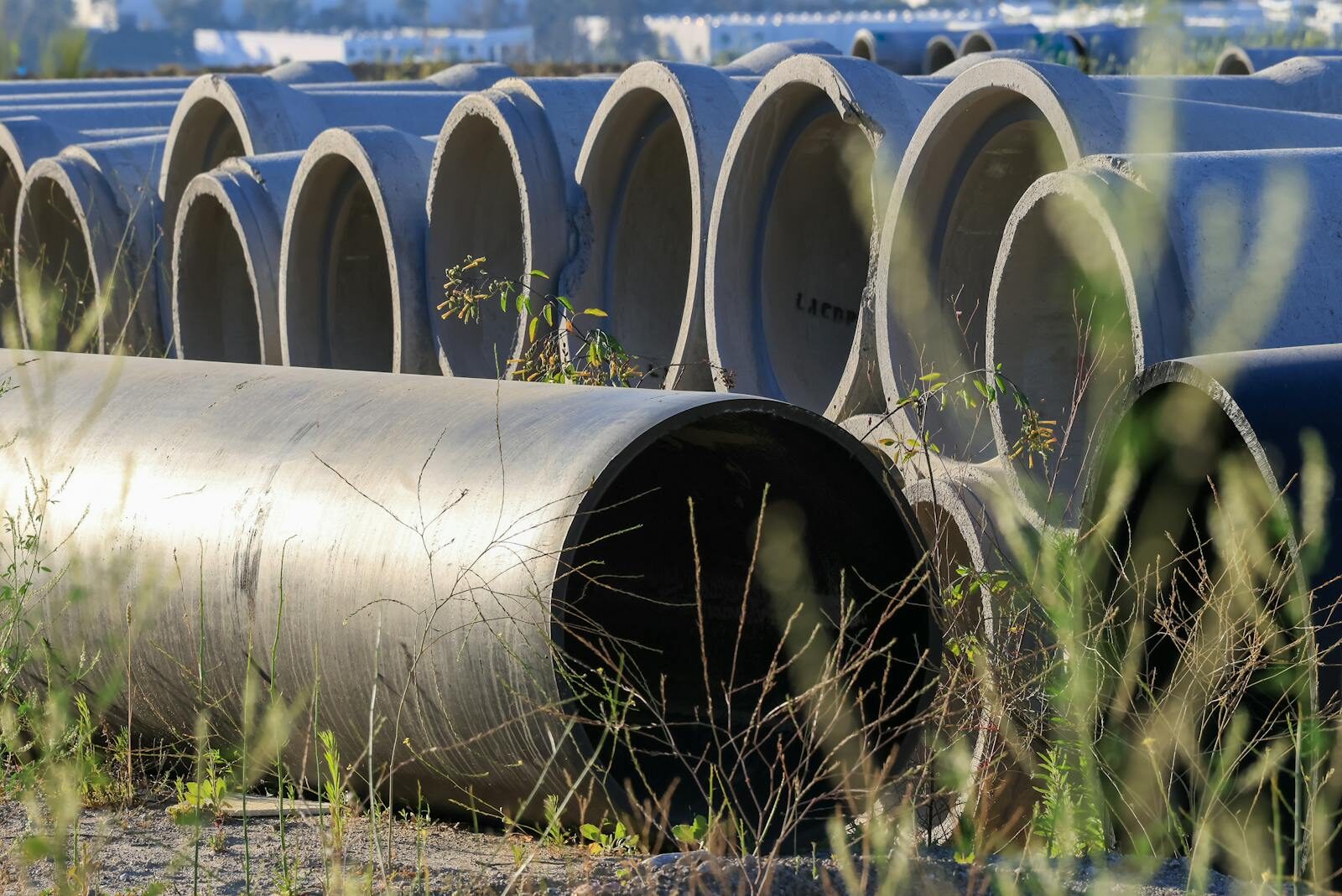 Photo by David Brown Stacked concrete pipes in an outdoor storage area surrounded by grass.