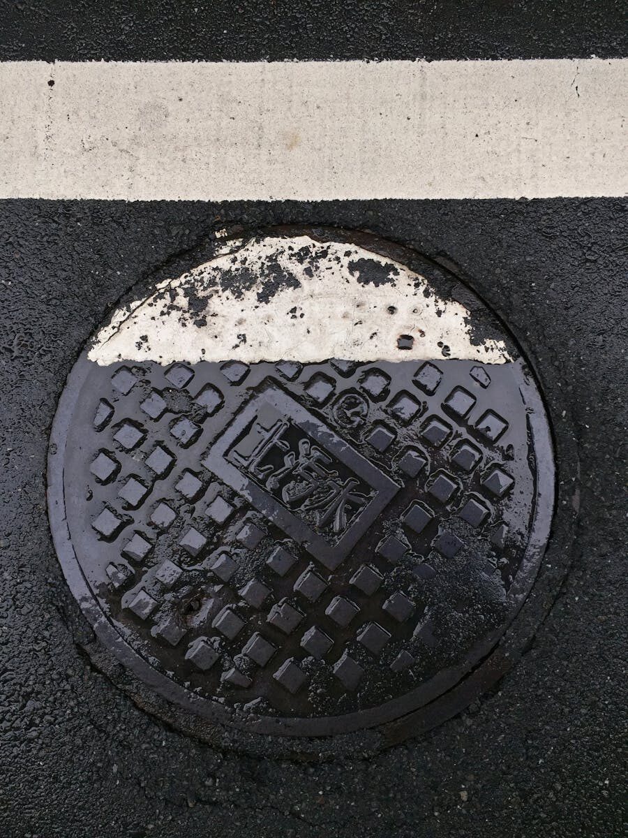 Close-up of a wet manhole cover partially covered by a road line in Taipei, Taiwan.