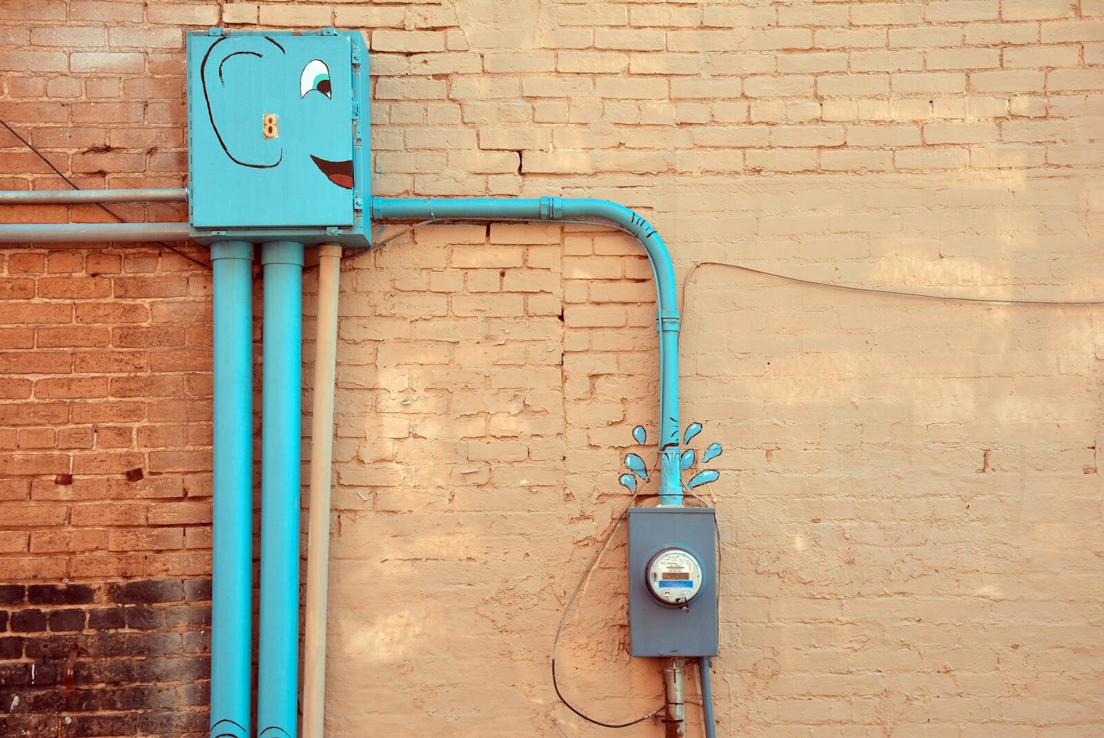 A quirky outdoor scene featuring painted utility meters and piping on a brick wall in Texarkana, Texas.