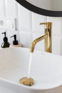 Gold faucet pouring water into a sleek modern sink with tile background.