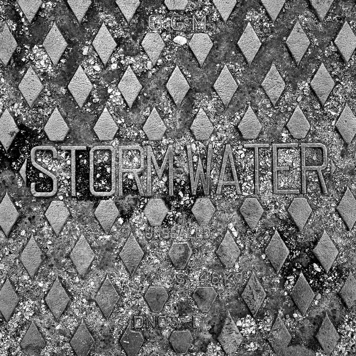 Detailed view of a metallic storm water drain cover with textured pattern.