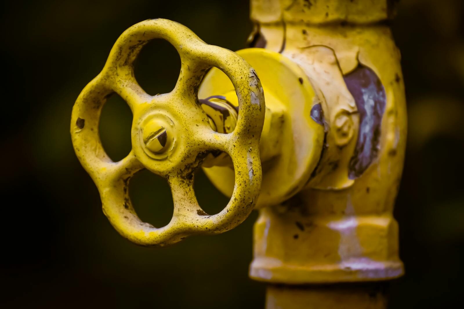 Close-up view of a rusty yellow shut-off valve, emphasizing industrial wear.