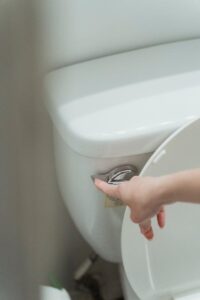 Close-up of a hand flushing a modern toilet, emphasizing hygiene and water conservation.