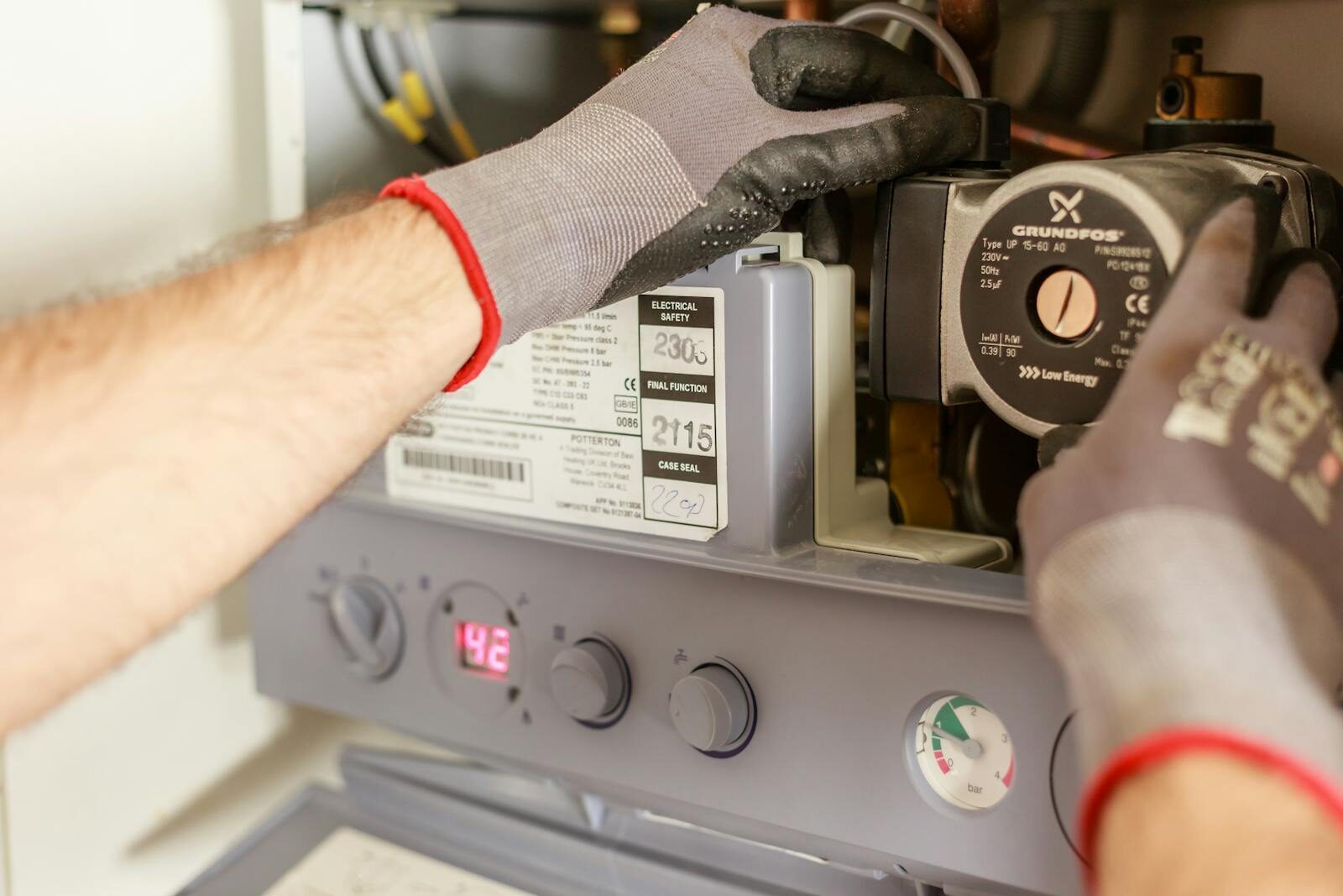 Photo by Heiko Ruth Close-up of hands adjusting a boiler system with precise instrumentation, showing maintenance work.