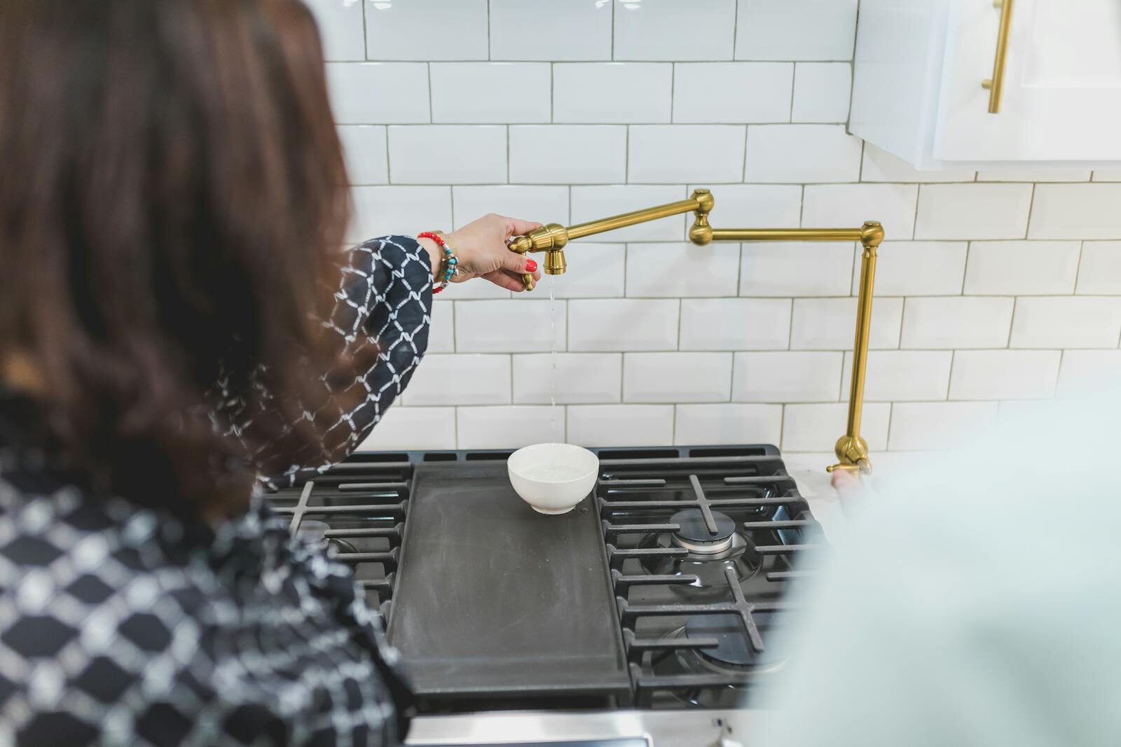 A person demonstrating the use of a brass kitchen faucet over a stove in a modern home kitchen.