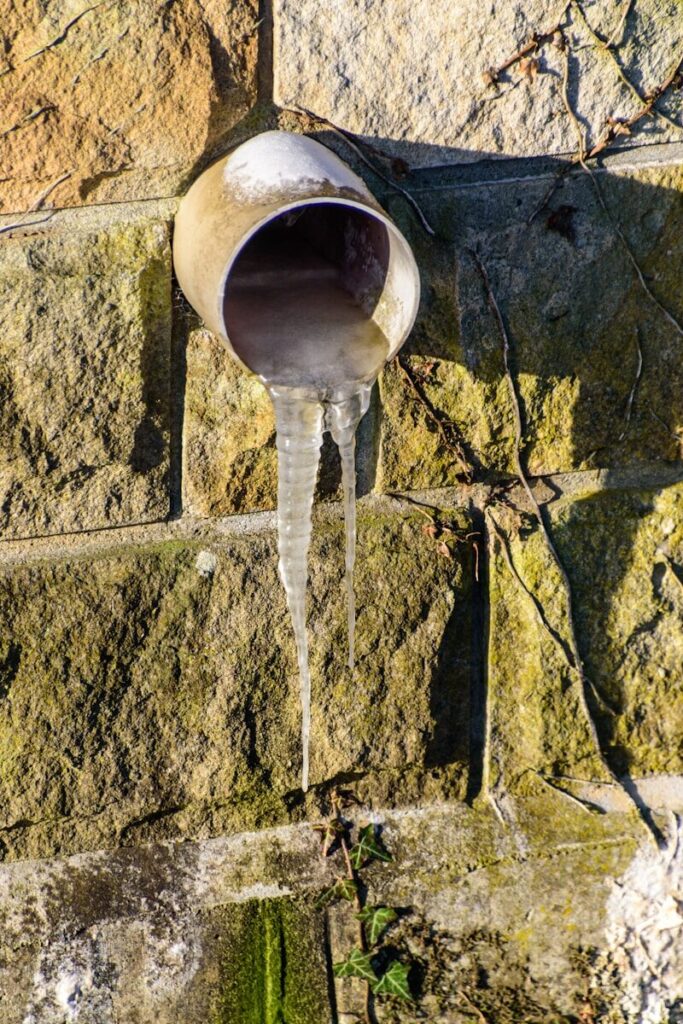 Icicles hang from a pipe on a stone wall