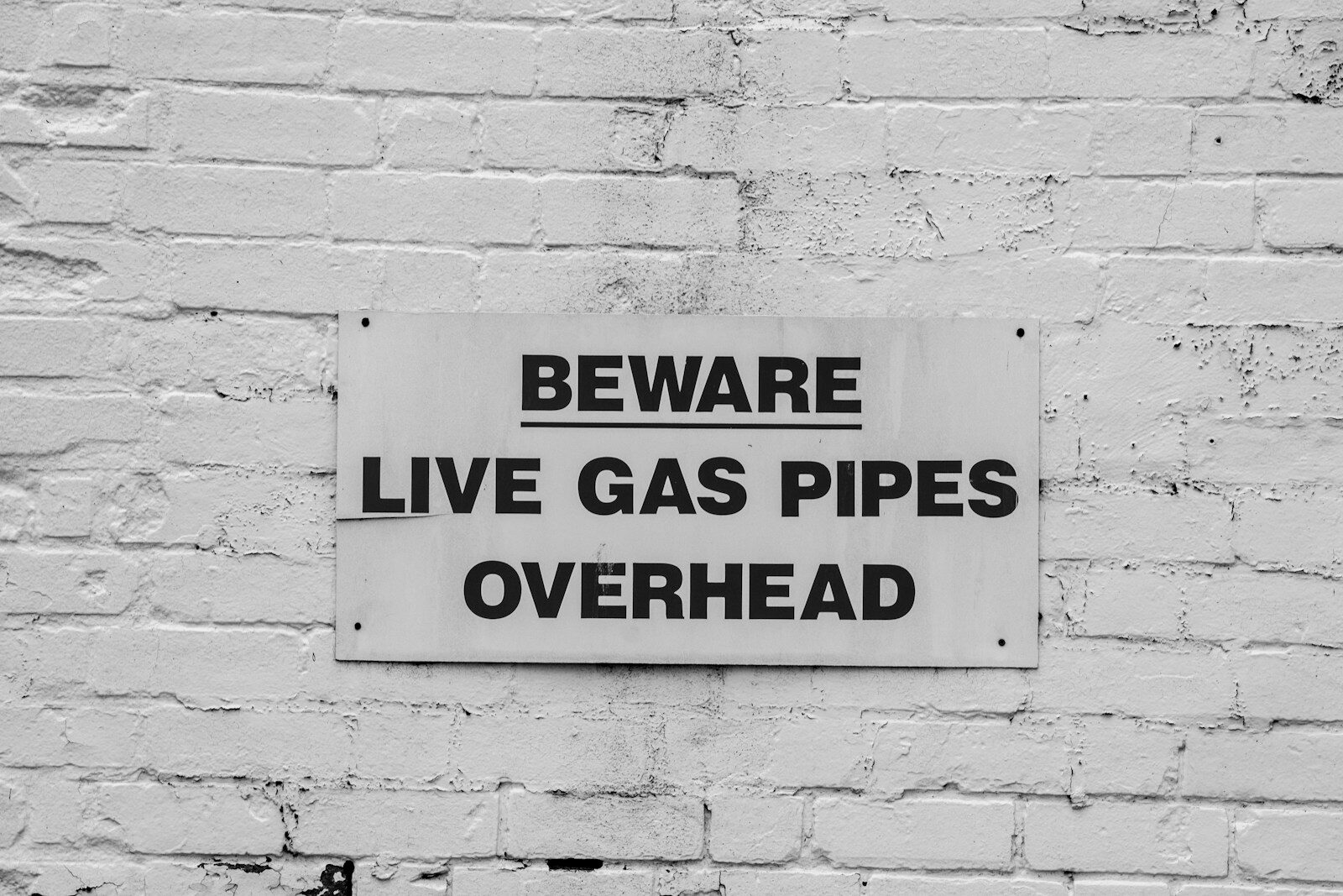 Photo by Richard Bell A brick wall with a sign on it stating beware live gas pipes overhead