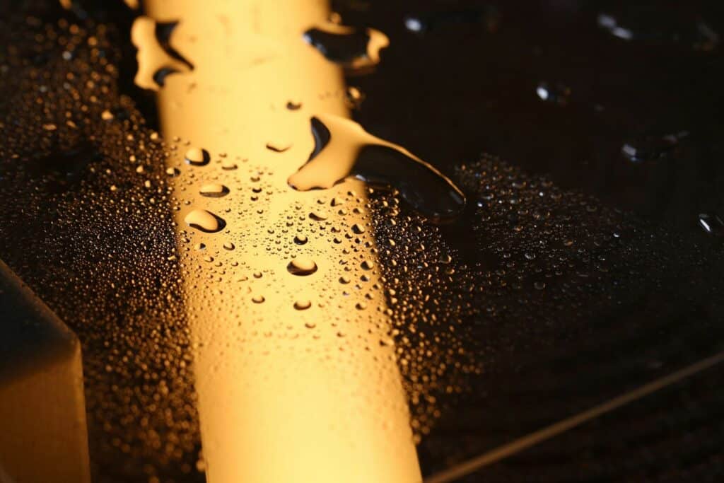 Golden light illuminates water droplets on a dark surface.