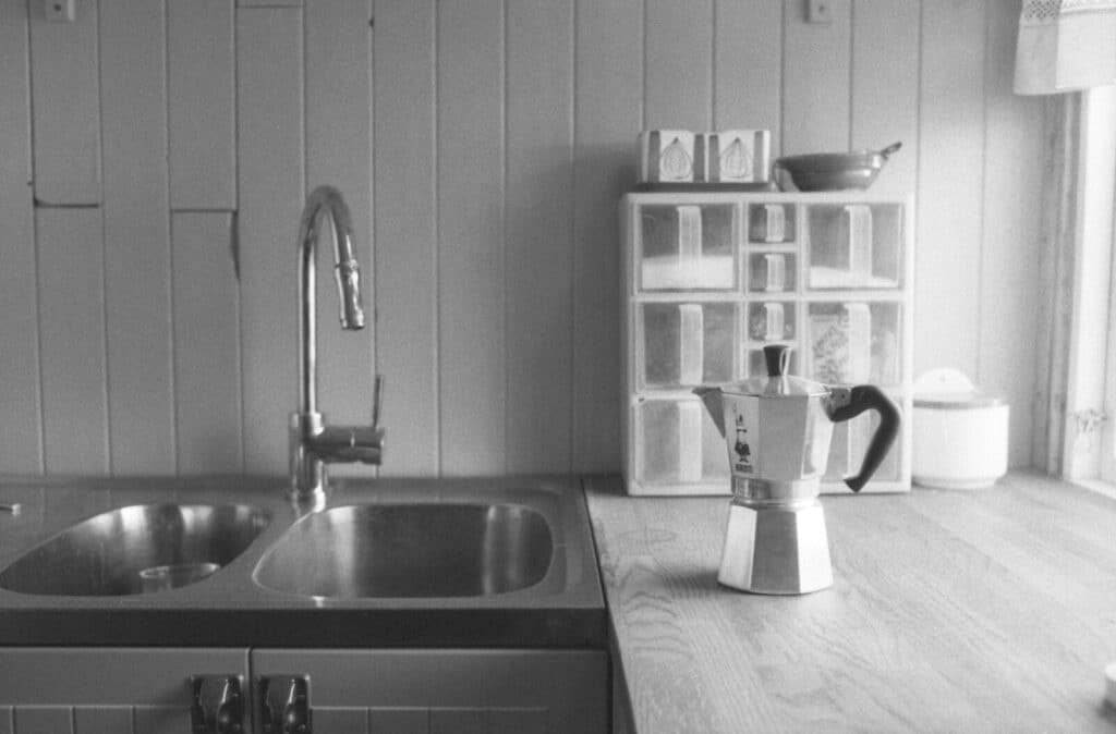 A moka pot on a wooden kitchen counter beside a stainless steel sink.