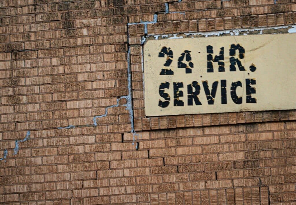 A weathered brick wall with a sign reading "24 HR. SERVICE" and cracks
