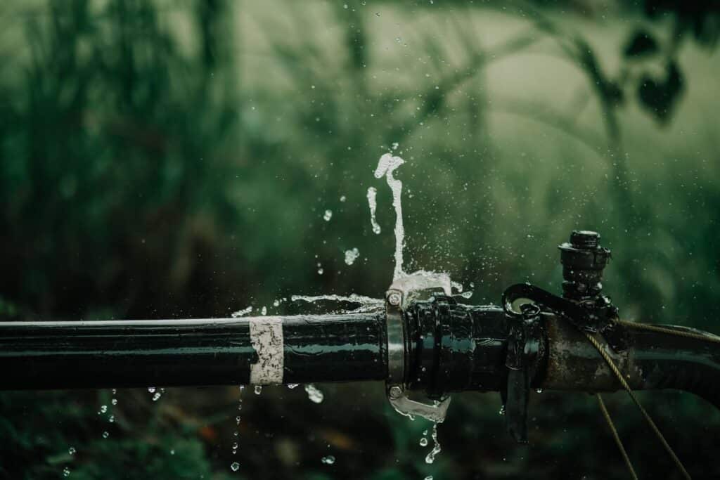 A detailed view of a leaking water pipe in a lush green garden setting.